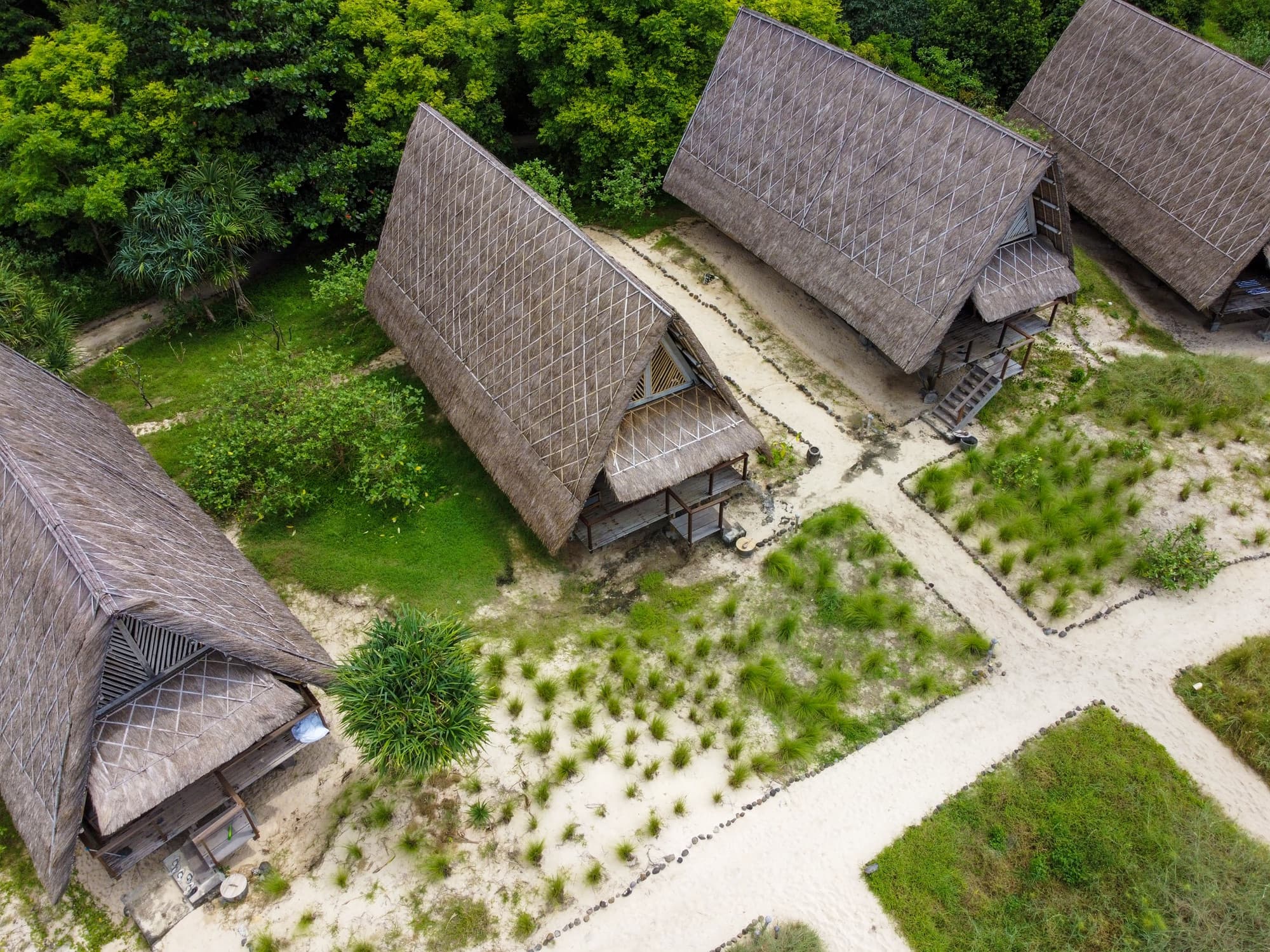 Top-down aerial view of three A-frame lodges nestled in tropical forest above the beach