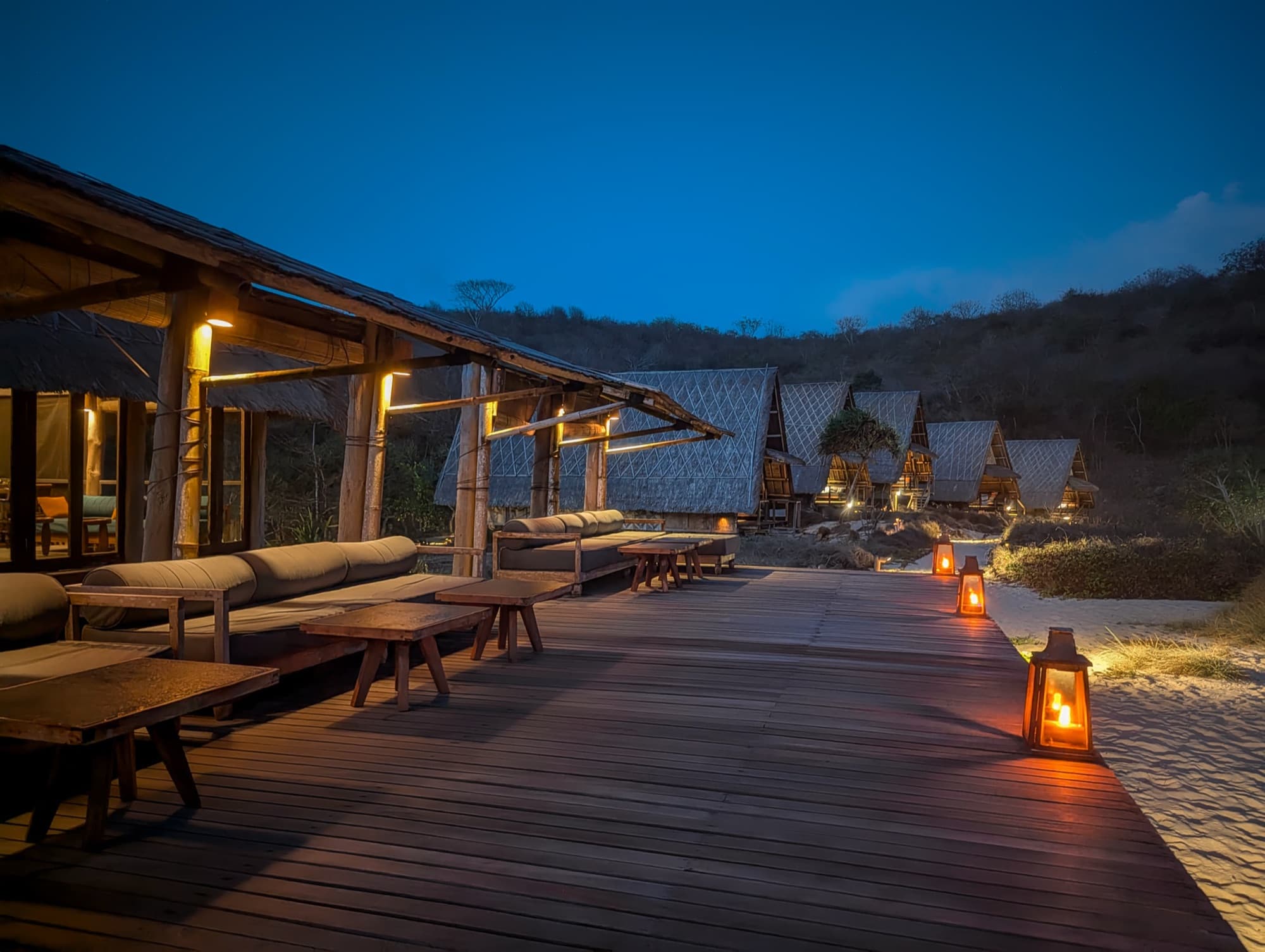 Wooden boardwalk lined with candle lanterns at dusk, leading toward the lodges