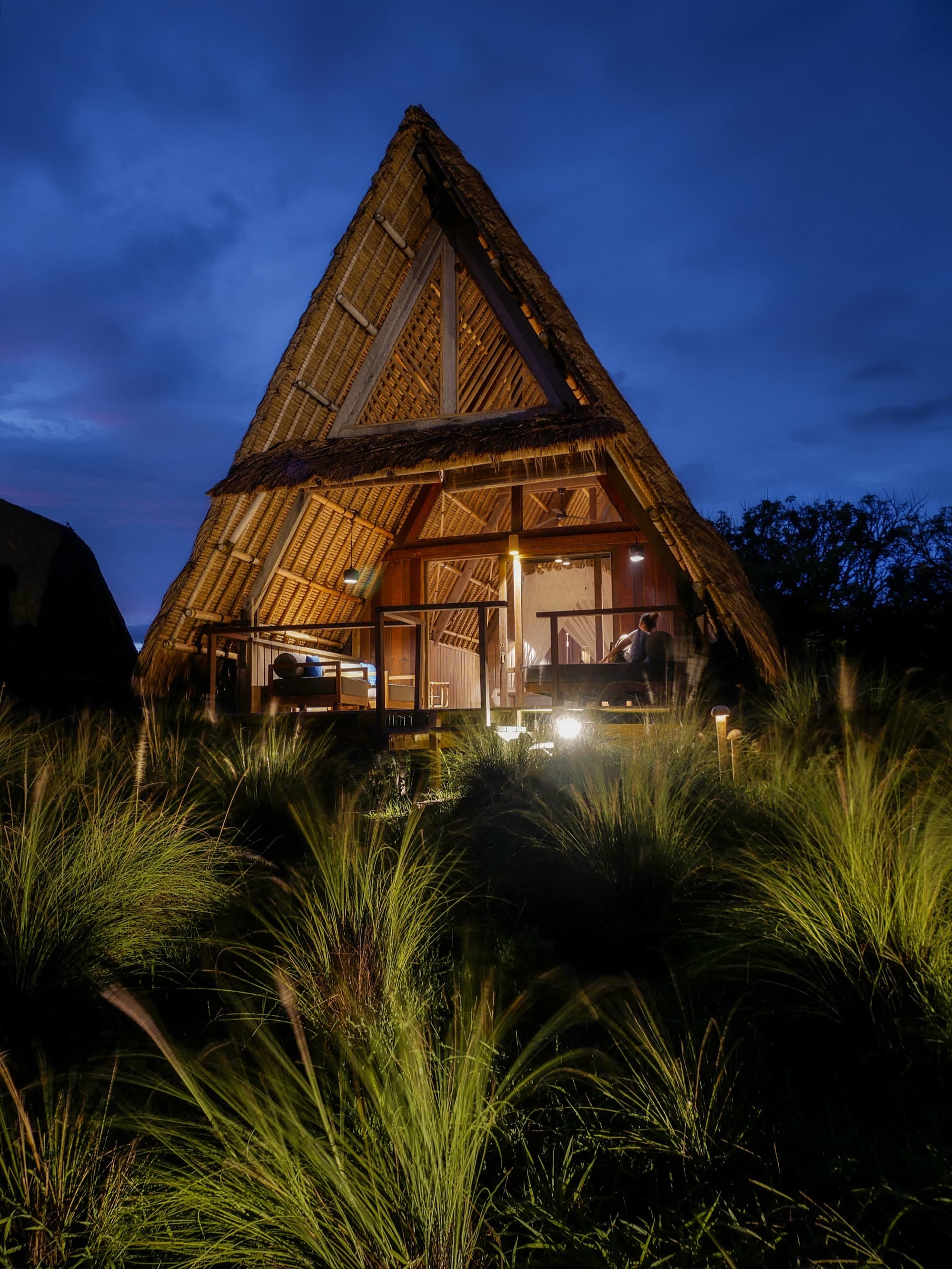 A-frame lodge lit from within at night on the remote Tanjung Ringgit beach