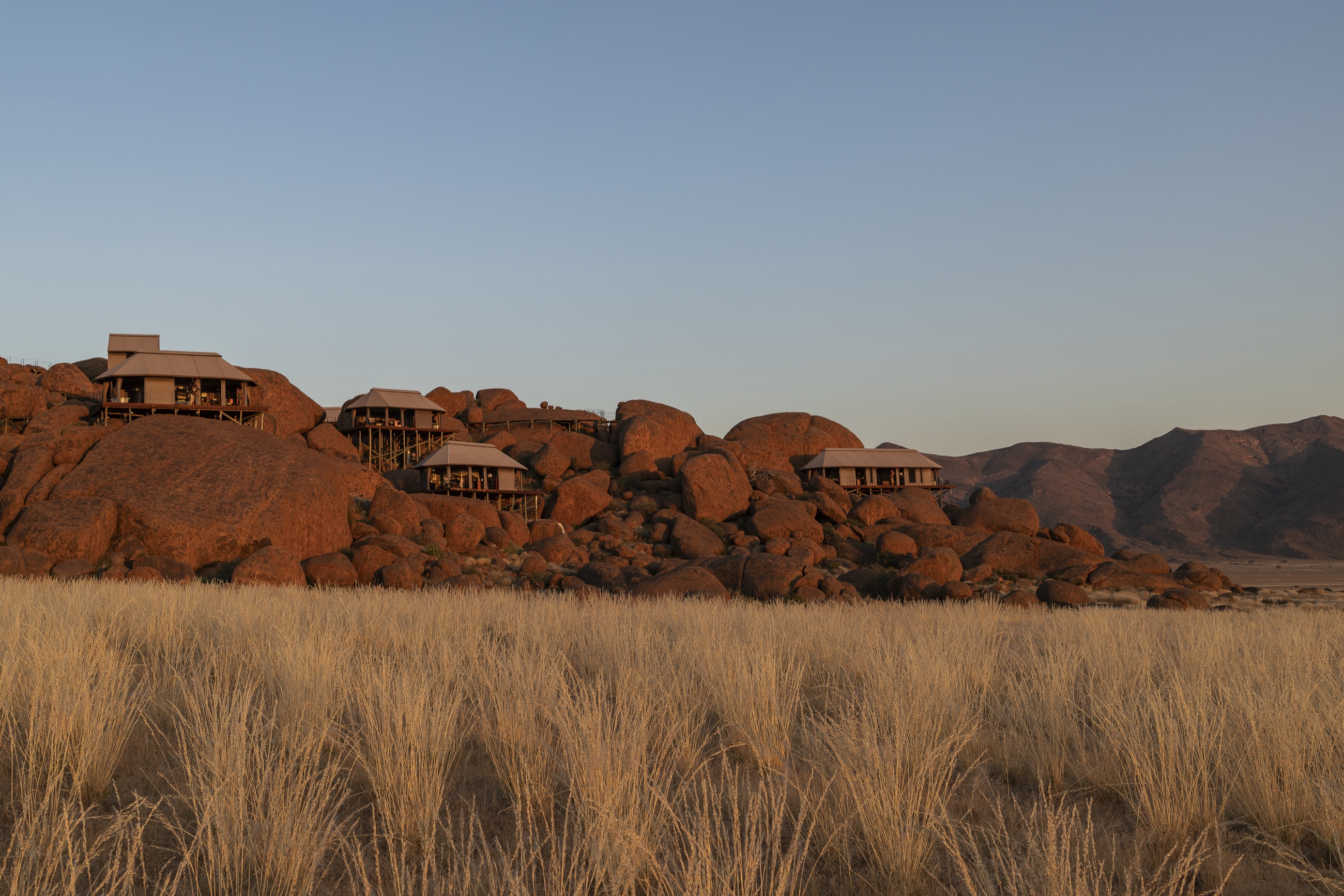 Tents on stilts among granite boulders above golden grass — Zannier Sonop, southern Namib Desert, Namibia